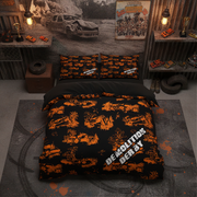 A bed dressed in a black and orange racing-themed bedding set with tank prints and 'DEMOLITION DERBY' text, styled in a rustic workshop-like bedroom with racing decor and shelves.