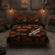 A bed dressed in a black and orange camouflage-patterned bedding set with 'DEMOLITION DERBY' printed in white, styled in a rustic garage room setting.