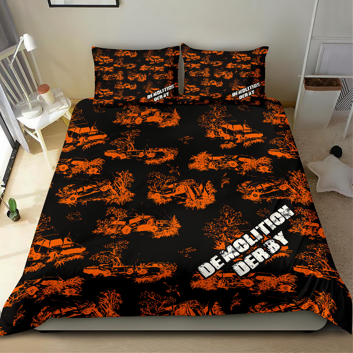 A made bed in a bedroom setting featuring a black bedding set with an orange graffiti-style pattern of demolished cars and the words 'DEMOLITION DERBY' in white. The room includes a white chair, side table, and shelving.