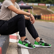 A person sitting on a racetrack curb wearing green and black graphic sneakers with white soles, paired with a beige t-shirt and black cargo pants.