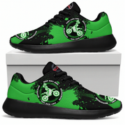 A pair of low-top sneakers shown from the side, with one shoe resting on top of a white box and the other below. The shoes have a bright green and black paint-splatter design with a circular graphic featuring a dirt bike rider and the text 'DIRT BIKER GIRL' and 'MOTOROGAS'.