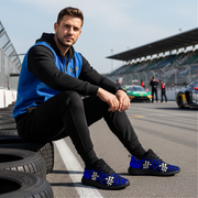 Man sitting on a race track with dirt racing sneakers, surrounded by tires and racing cars.