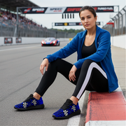 Woman sitting on a race track with a car in the background wearing a checkered blue muddy sneakers