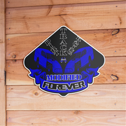 A die-cut vinyl sticker featuring a blue and black graphic of two sports cars with the text 'Dirt TRACK Racing MODIFIED FOREVER', displayed on a light brown wooden plank background.