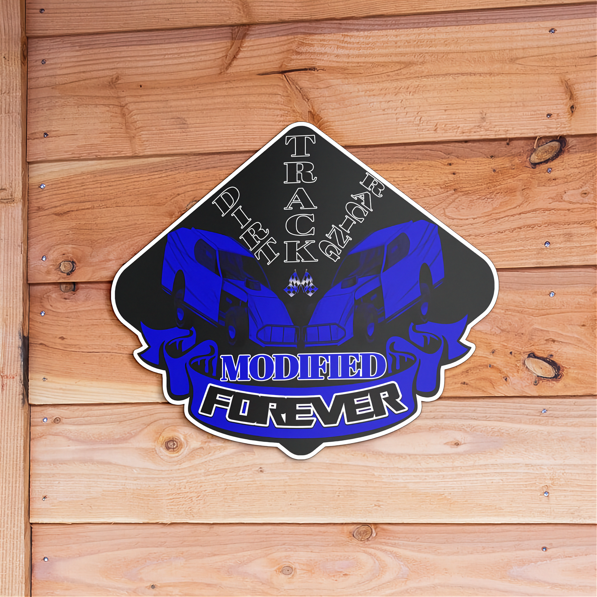 A die-cut vinyl sticker featuring a blue and black graphic of two sports cars with the text 'Dirt TRACK Racing MODIFIED FOREVER', displayed on a light brown wooden plank background.