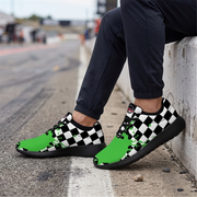 A person sitting on a concrete barrier wearing black and white checkered sneakers with bright green accents, paired with dark navy pants, on an asphalt surface.