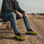 Man sitting on a bench wearing black and yellow checkered shoes in an outdoor setting.