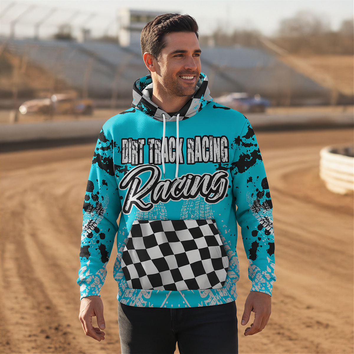 A man wearing a bright turquoise hoodie with 'DIRT TRACK RACING Racing' printed across the front, featuring a black-and-white checkered graphic on the kangaroo pocket and black splatter details on the sleeves, standing on a dirt racetrack.