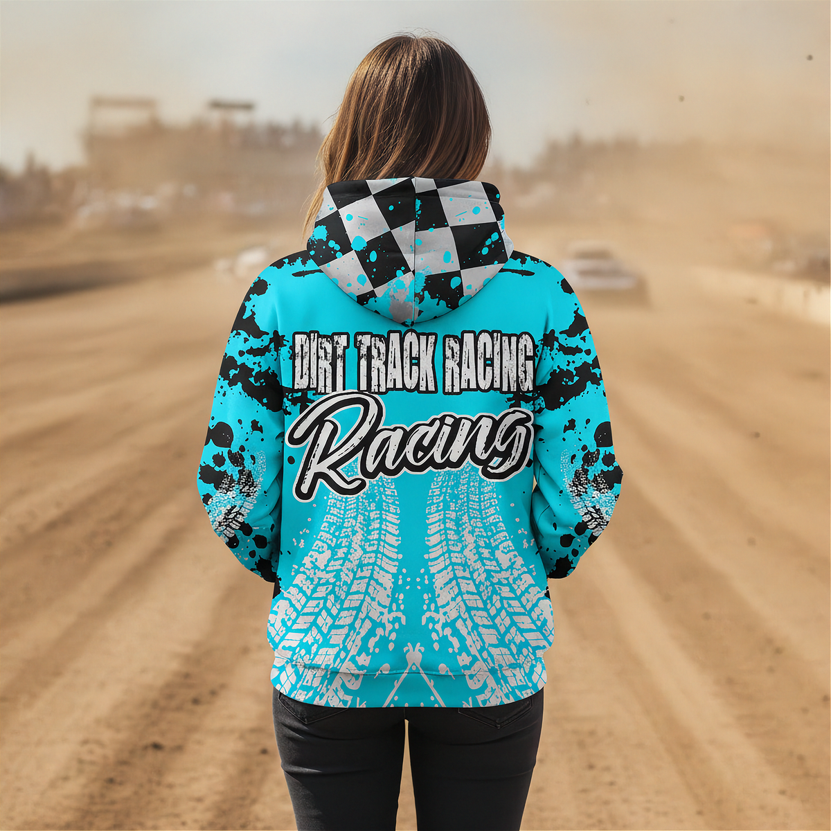 A woman standing on a dirt track wearing a bright turquoise hooded sweatshirt with black splatter graphics, a black-and-white checkered hood, and large 'DIRT TRACK RACING Racing' text across the back. The background shows a blurred dusty racetrack scene.