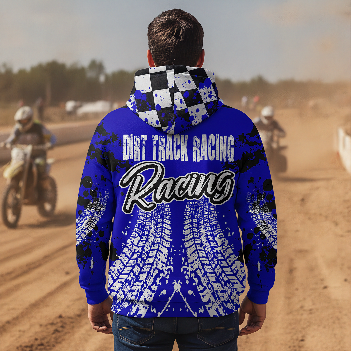 A man viewed from behind wearing a royal blue hoodie with a black and white checkered hood and a graphic print of tire tracks and the words 'DIRT TRACK RACING Racing' on the back. The background shows a blurred dirt track scene with motocross riders.