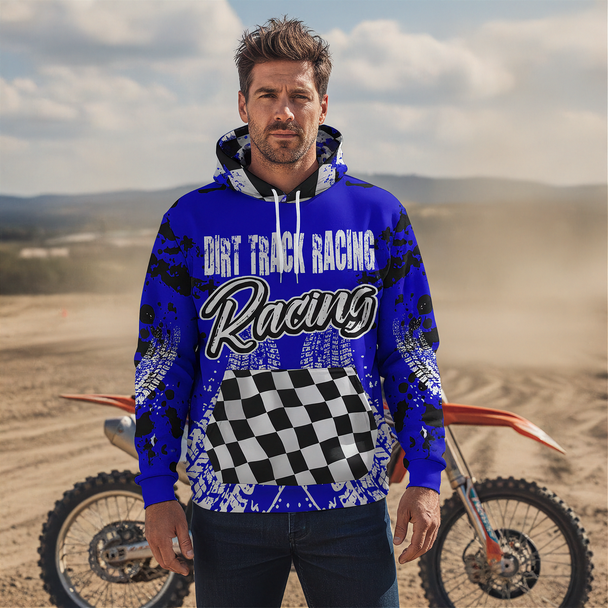 A man wearing a blue and black 'Dirt Track Racing' hoodie stands in a dusty outdoor desert setting with a dirt bike behind him.