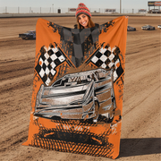 Woman holding a racing-themed blanket with a car and checkered flags design at a dirt track.