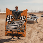 Man holding a racing-themed blanket on a dirt track with cars in the background