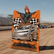 Woman holding a large orange blanket with car and checkered flag design on a race track.