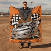 Man holding a blanket with a car and checkered flag design on a dirt track.