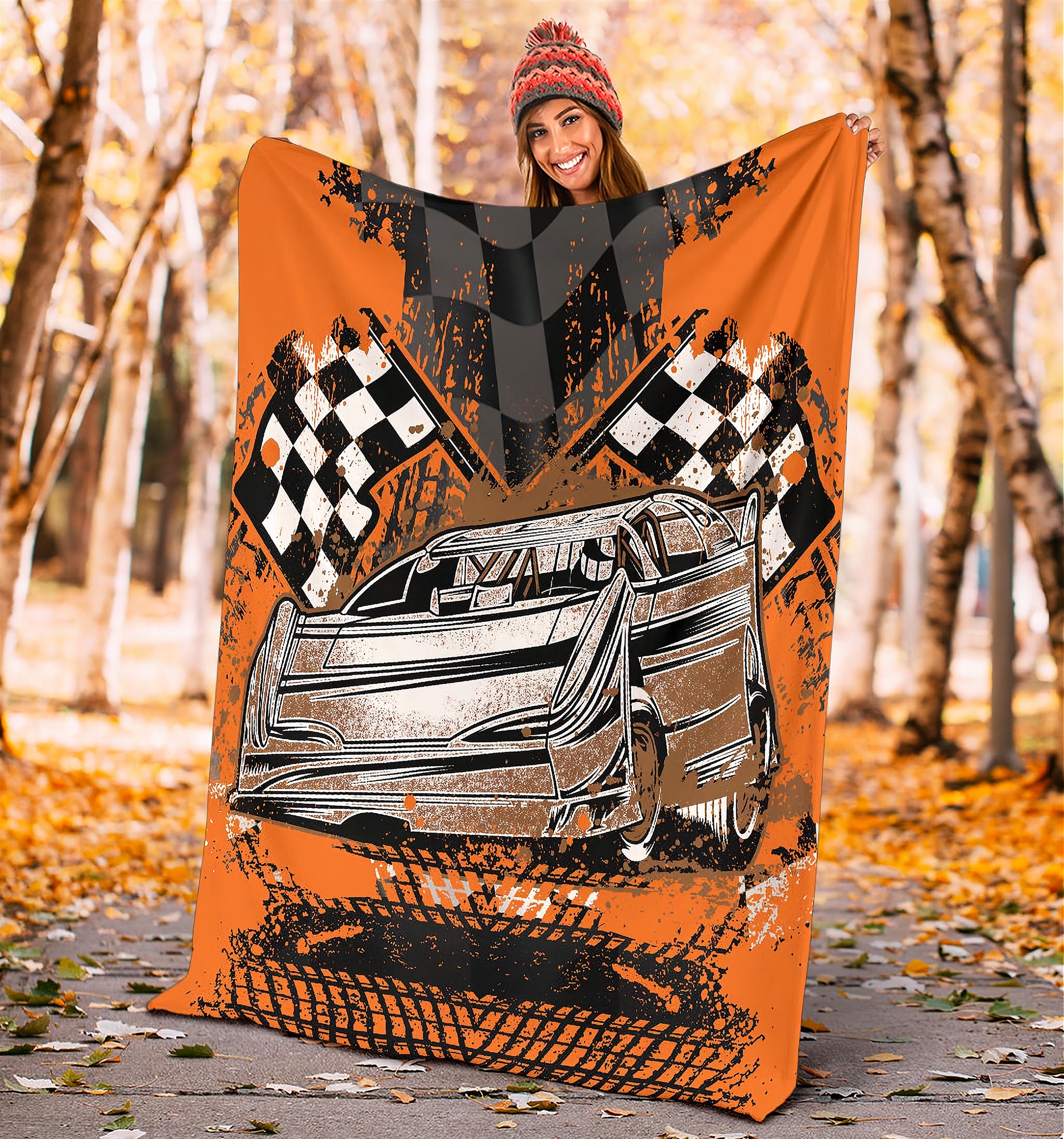 Woman holding a racing-themed blanket with a car and checkered flags design in an autumn setting.