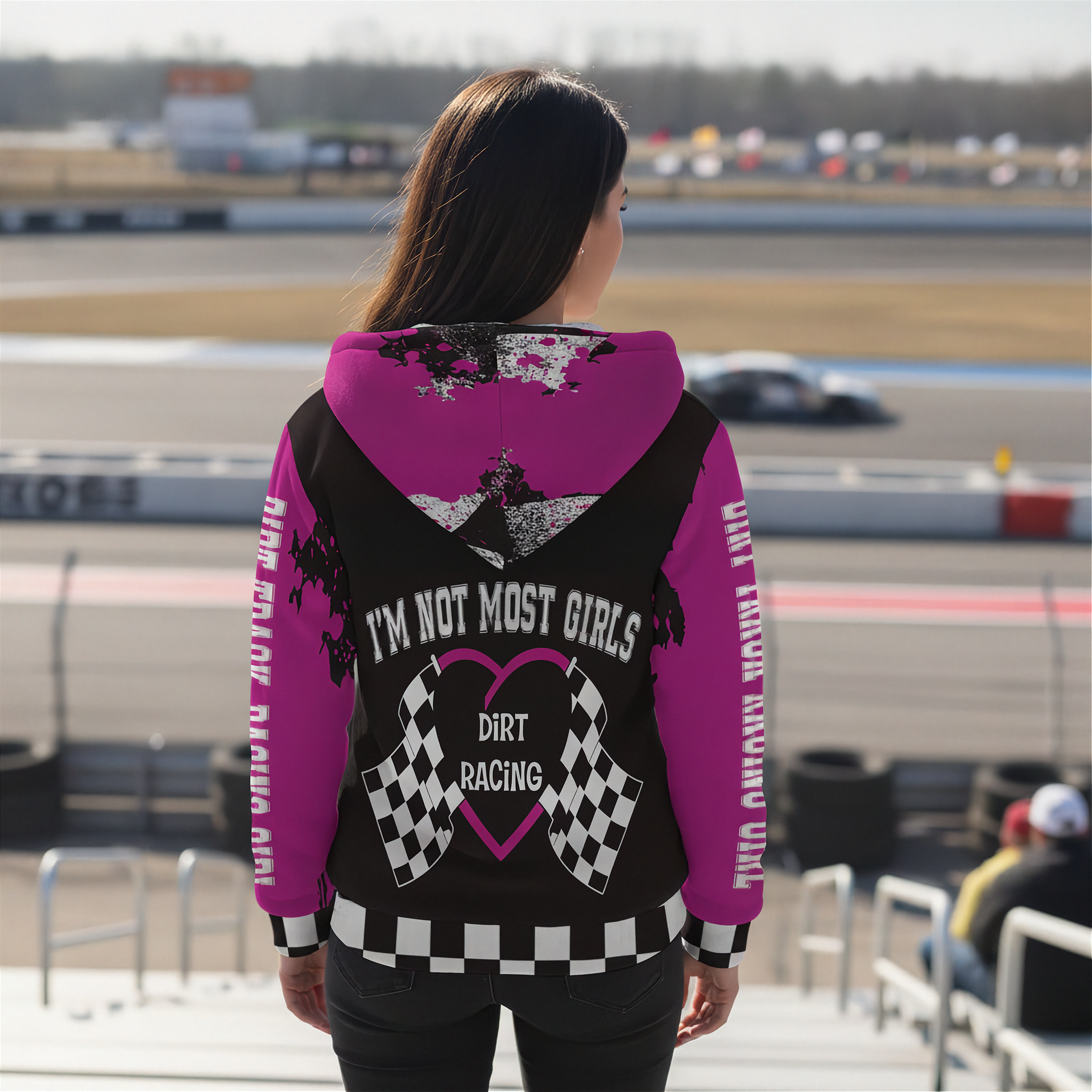 Person wearing a pink and black hoodie with text at a race track