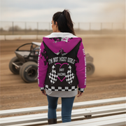 Woman wearing a pink sherpa hoodie with 'I'm Not Most Girls Dirt Racing' text at a race track.