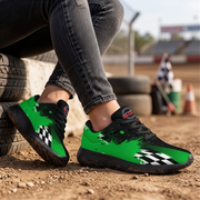 A pair of black and bright green racing-inspired sneakers worn by a person sitting outdoors on a dirt track, with tires and a blurred background visible.