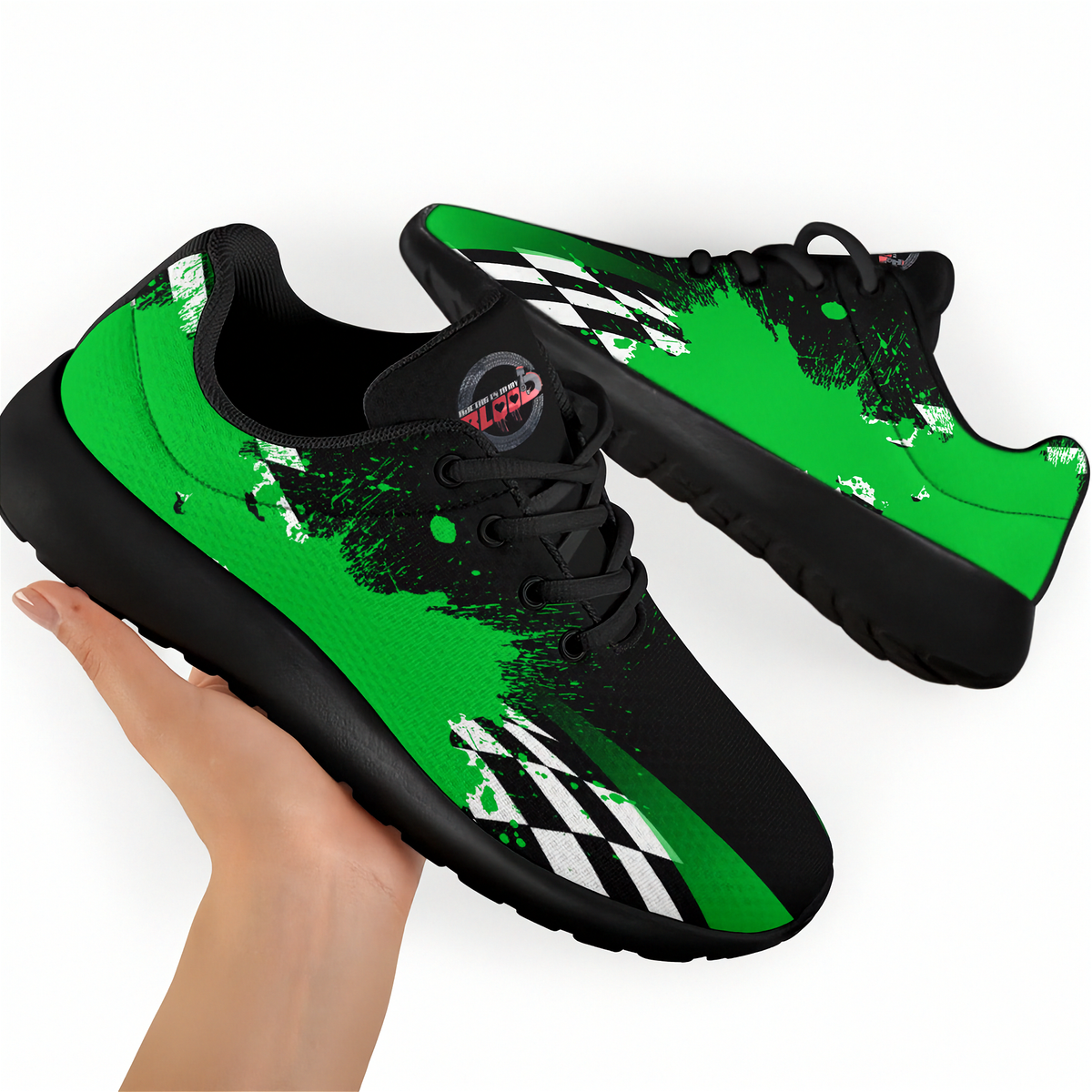 A pair of low-top athletic sneakers in black and bright green with a white checkered stripe detail and black laces, shown with one shoe being held by a hand against a plain white background.