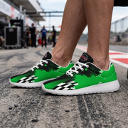 A pair of low-top sneakers worn on a person's feet, photographed on a racetrack. The shoes are bright green with black and white graphic patterns, white laces, and white soles.