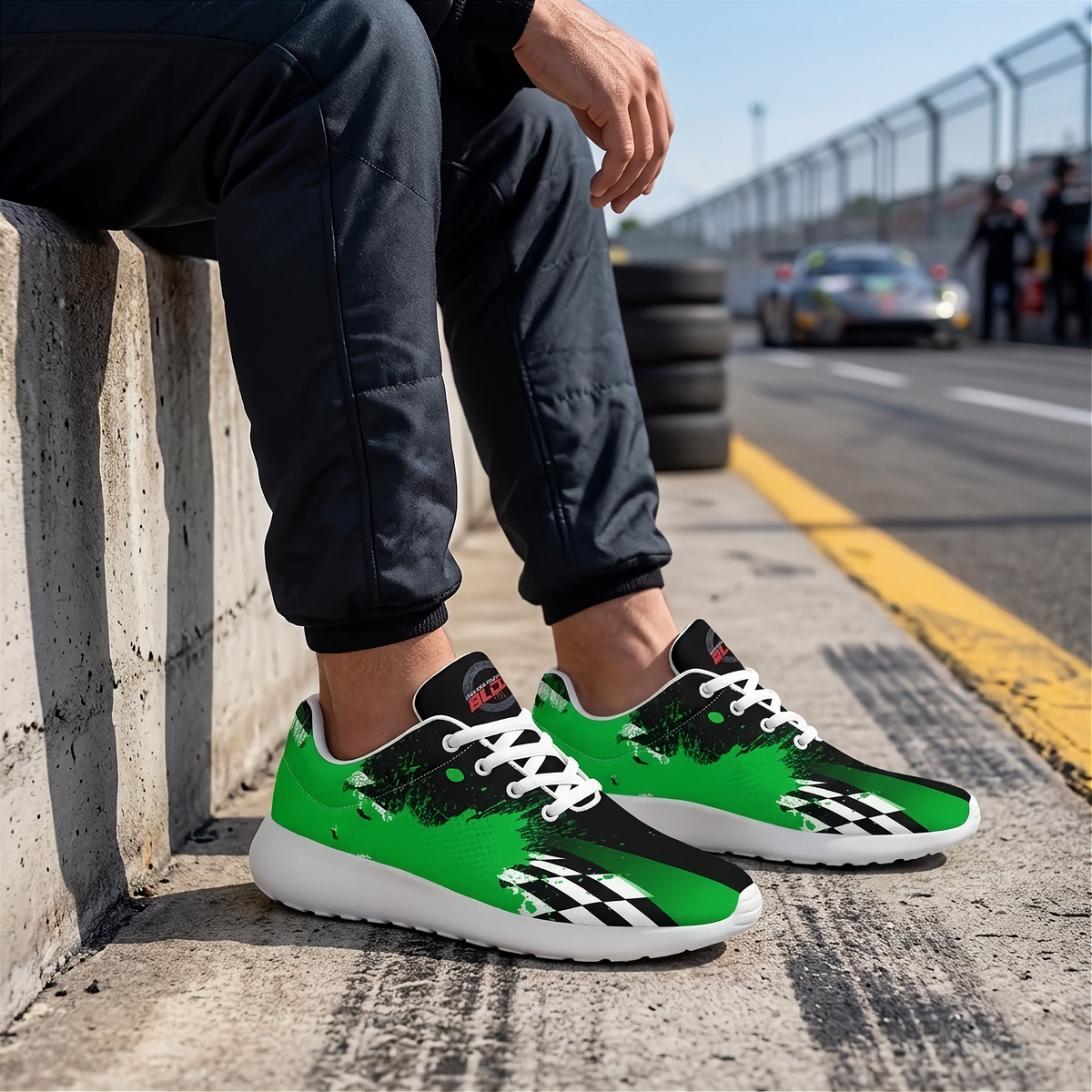 A person sitting on a concrete barrier at a racetrack wearing bright green and black checkered sneakers with white laces and white soles.