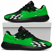 A pair of low-top athletic sneakers shown on a white background, with one shoe resting on top of a white box and the other in front. The shoes have a bright green and black design with white paint splatter details and a black-and-white checkered stripe near the front.