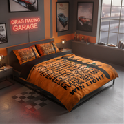 A bed dressed in an orange and black drag racing themed bedding set, styled in a modern garage-themed bedroom with a neon sign, car posters, and a checkered floor mat.