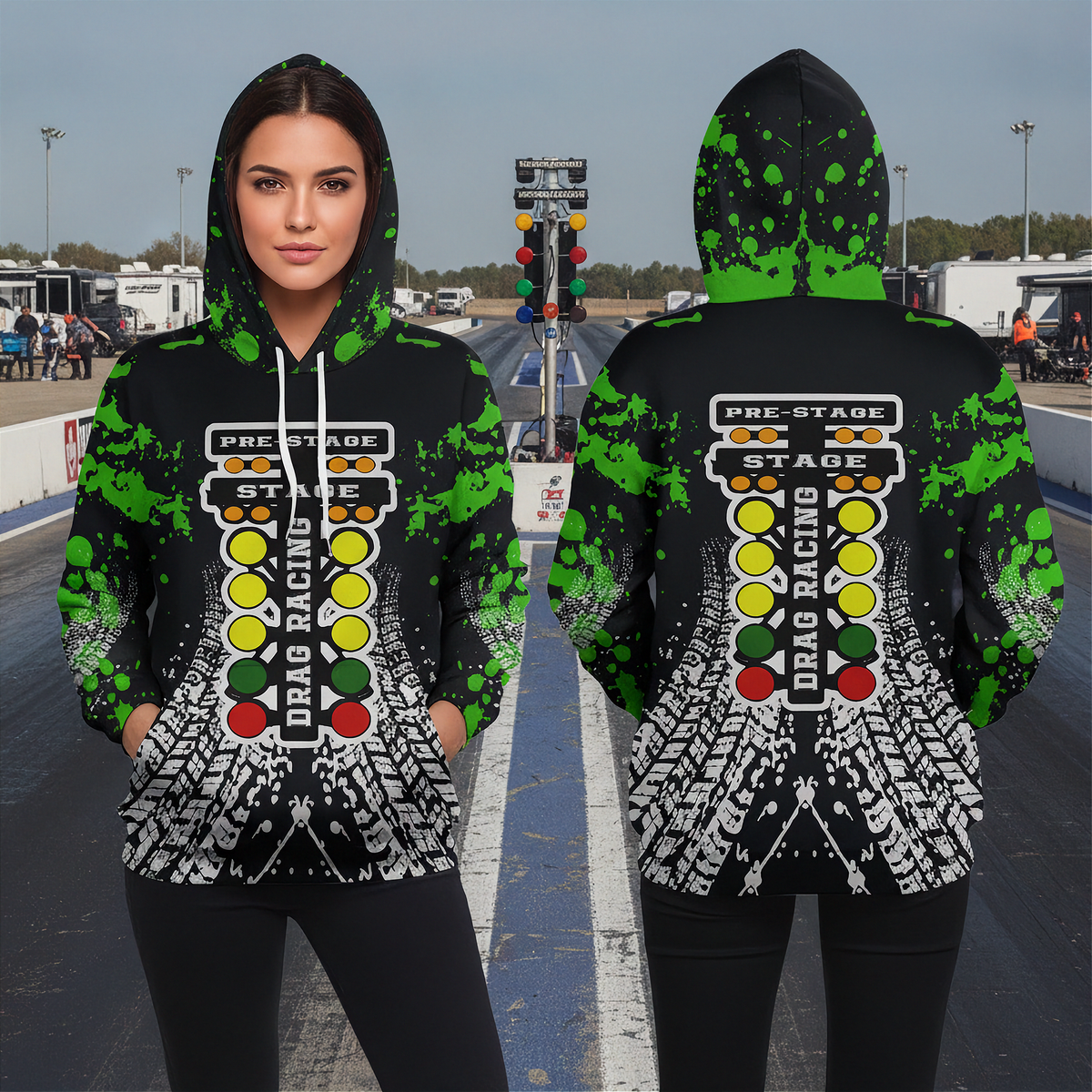 A woman wearing a black hoodie with a green, yellow, red, and white drag racing theme stands on a racetrack. The hoodie features a drag racing light column graphic and green paint splatters on the sleeves and hood.