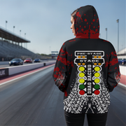 A person standing on a racetrack wearing a black hooded sweatshirt with a red splatter pattern and a large drag racing stage graphic on the back, shown from behind.