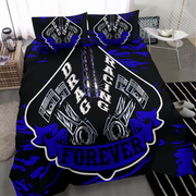 A black bedding set with a bold blue and white drag racing graphic, shown on a bed in a modern bedroom setting. The set includes a duvet cover and two matching pillowcases featuring a large shield design with pistons, chains, and the words 'DRAG RACING FOREVER'.