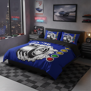 A blue racing-themed bedding set with a duvet cover and two matching pillowcases, displayed on a bed in a modern, dark-themed bedroom. The bedding features a large white tire graphic with smoke and red, yellow, green, and blue oval accents.