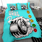 A bright turquoise bedding set featuring a large drag racing tire graphic with smoke and the words 'DRAG Racing,' plus matching pillowcases. The set is shown on a bed in a styled bedroom with a chair, side table, rug, and slippers visible.
