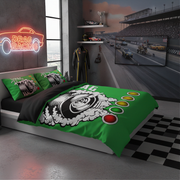 A racing-themed bedding set displayed on a bed in a modern, dark-themed racing simulator room. The set includes a vibrant green duvet cover and matching pillowcases featuring a black and white tire graphic with red, yellow, and green signal lights.