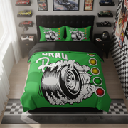 A racing-themed bedding set featuring a bright green duvet cover and matching pillowcases with a large black-and-white tire graphic, smoke, and the words 'DRAU Racing.' The set is styled on a bed in a modern bedroom with racing wall decor, shelves, and a checkered floor.
