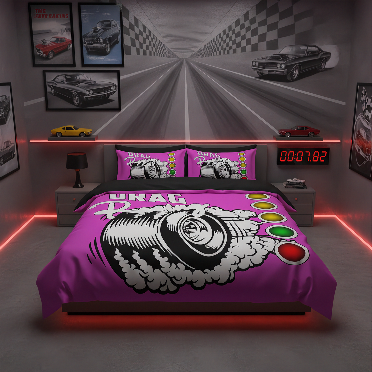 A bedroom setup featuring a bed dressed in a bright pink racing-themed bedding set with a large tire graphic and track number print. The room has gray walls, framed car posters, two gray nightstands, red LED lighting strips, and a digital stopwatch on the headboard.
