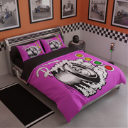 A racing-themed bedding set on a bed in a styled bedroom. The set includes a bright pink duvet cover and two matching pillowcases, all printed with a large black-and-white tire graphic, speed lines, and racing light accents.