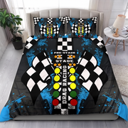 A racing-themed bedding set featuring a duvet cover and two matching pillowcases on a bed. The design includes black and white checkered flags, a central striped finish-line motif with yellow, orange, green, and red lights, and blue paint splatters on a black background.