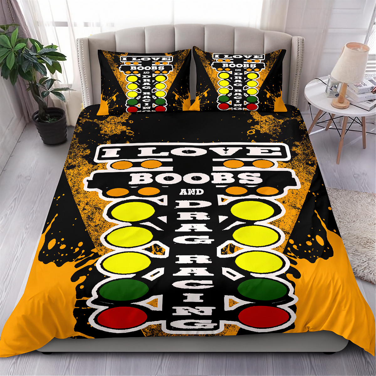A made bed in a bedroom setting featuring a bold novelty bedding set with a black, yellow, orange, green, and red graphic design. The design includes the text 'I LOVE BOOBS AND DRAG RACING' alongside traffic light-style circles.