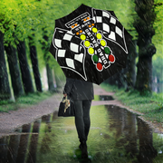 A person walking in the rain along a tree-lined path, holding a large black umbrella printed with a checkered flag design, colorful cherry blossoms, and the words 'Cherry Blossom Street Race.'.