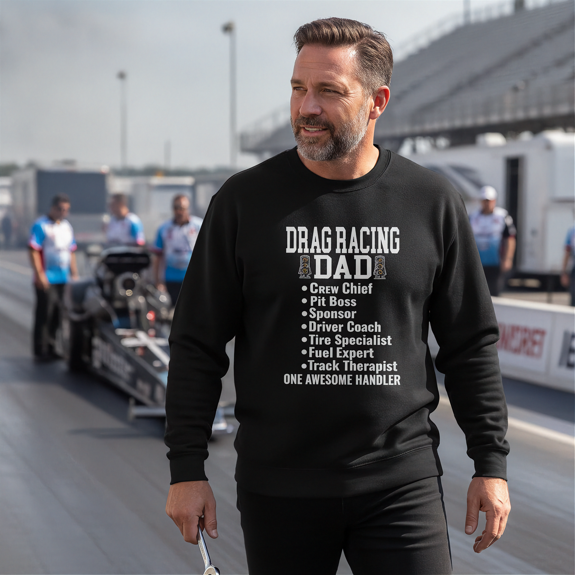 Man wearing a black sweatshirt with 'Drag Racing Dad' text at a race track.