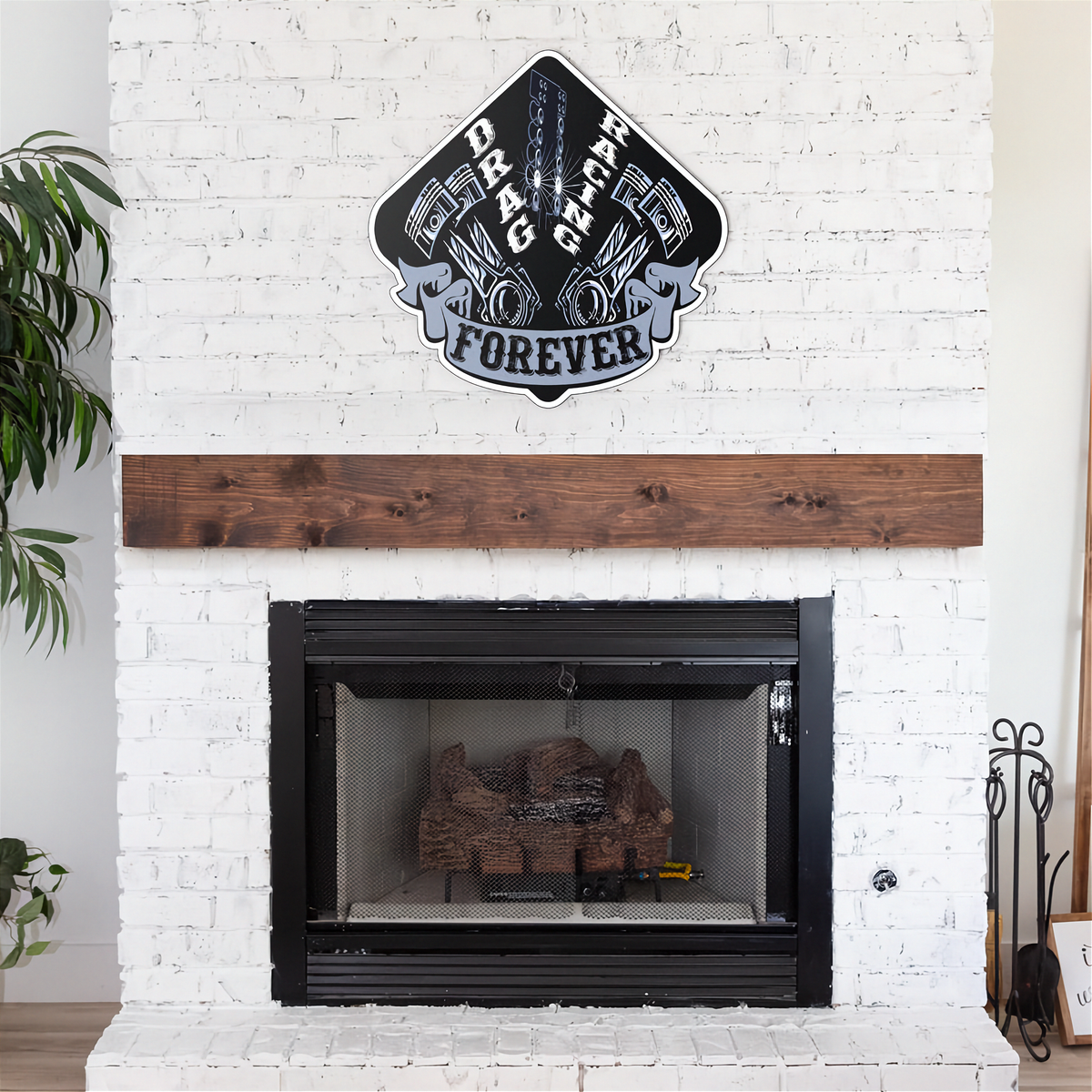 A decorative wall sign reading 'Drag Racing Forever' with pistons and chains, mounted above a black fireplace insert in a white brick wall with a wooden mantel.