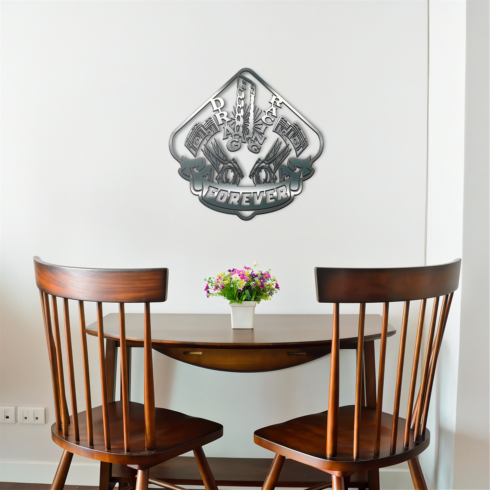 Wooden dining table with two chairs and a decorative drag racing metal wall art piece on a white wall.