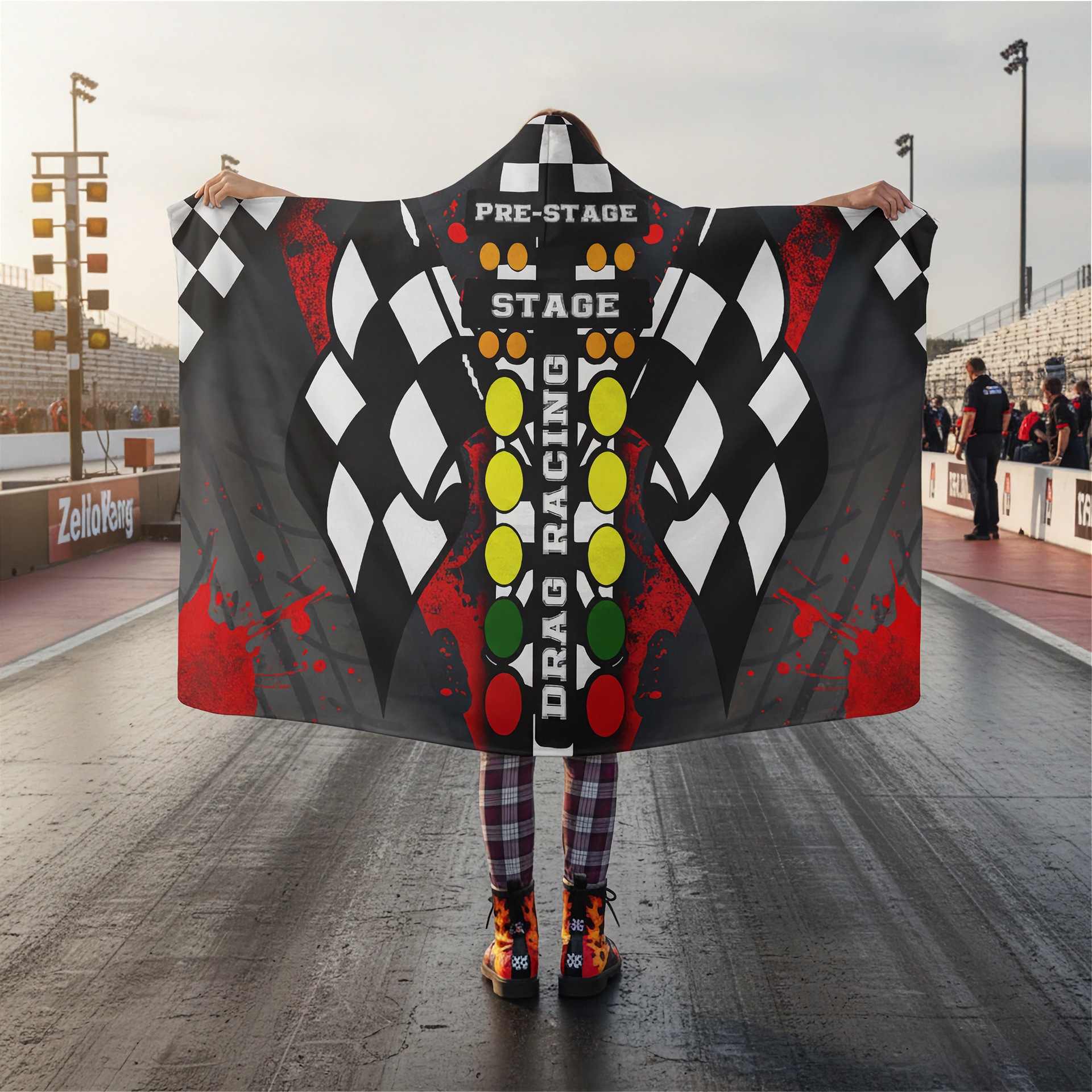 Person holding a large checkered flag hooded blanket with racing-themed design on a racetrack.