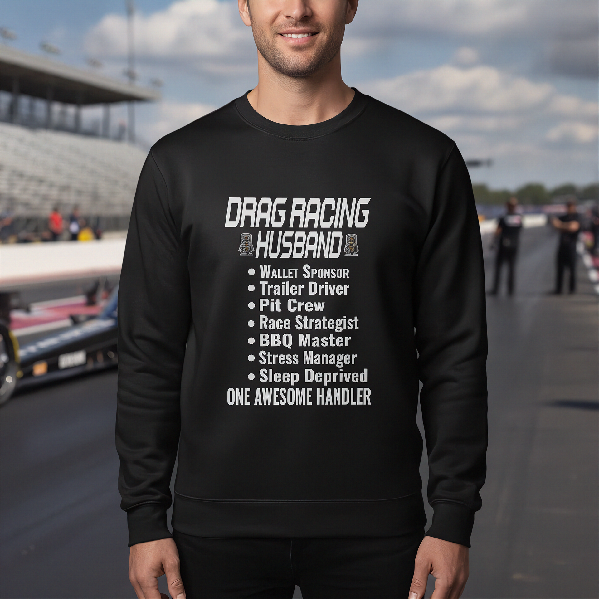 Person wearing a black sweatshirt with drag racing text at a race track.