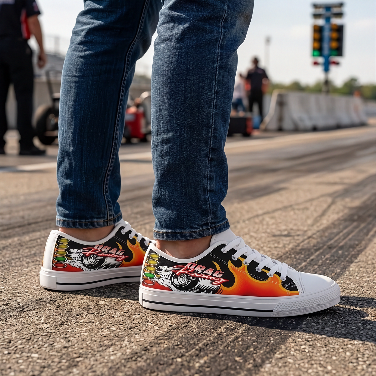 A person wearing blue jeans and white low-top sneakers with a colorful flame and racing graphic design, standing on an asphalt racetrack.