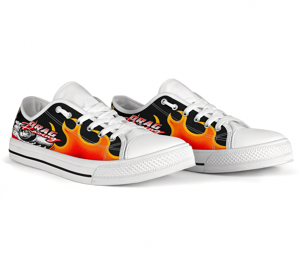 A pair of low-top white sneakers with black and orange flame graphics and 'DRAG' text on the sides, shown on a clean white background.