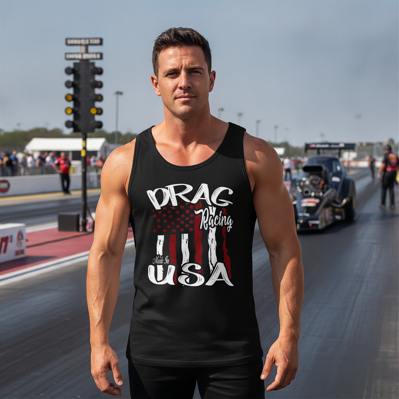 A muscular man stands on a drag racing track wearing a black tank top with a distressed American flag graphic and the words 'DRAG Racing USA'. A drag race car is visible in the background on the racetrack.