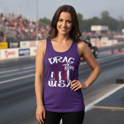 A woman stands on a racetrack wearing a purple racerback tank top with a patriotic graphic that reads 'DRAG Racing USA' in white, red, and blue. The background shows a blurred racetrack and grandstands.