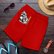 Red men's shorts with a 'Drift Racing' tire graphic and traffic light design, styled in a flat lay on a dark wood background with sunglasses, a straw hat, flip-flops, and a watch.